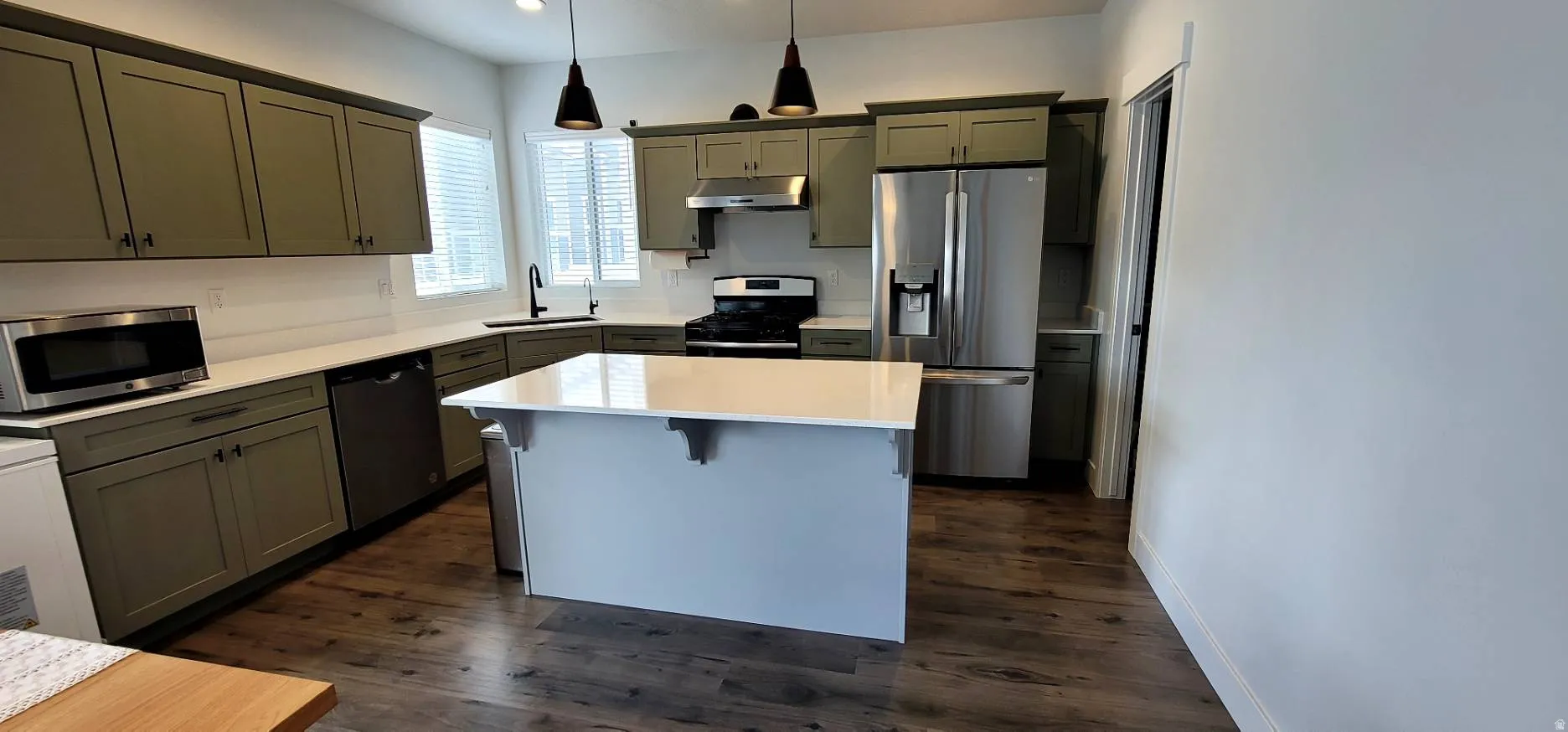 Kitchen featuring stainless steel appliances, pendant lighting, dark wood-style floors, gray cabinets, and a center island