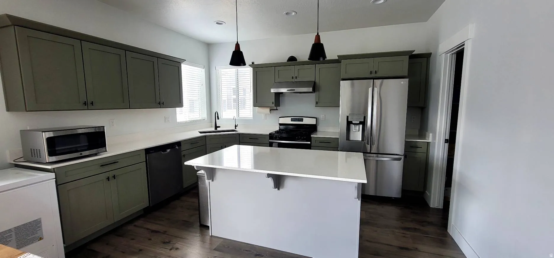Kitchen with stainless steel appliances, hanging light fixtures, dark wood-style flooring, and a center island