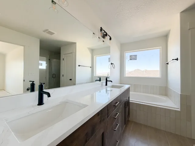 Spacious bathroom featuring a dual vanity with integrated sinks and matte black fixtures, a built-in soaking tub, a large window, and tile flooring