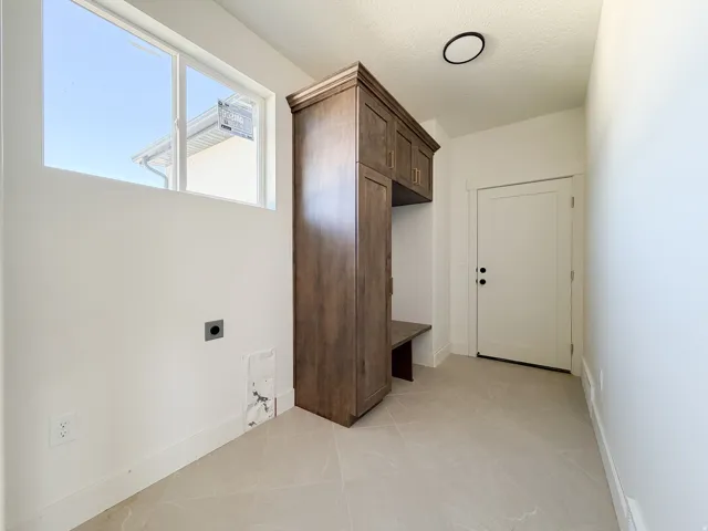 Mudroom with built-in wood-finish cabinetry, integrated bench seating, and light-toned tile flooring