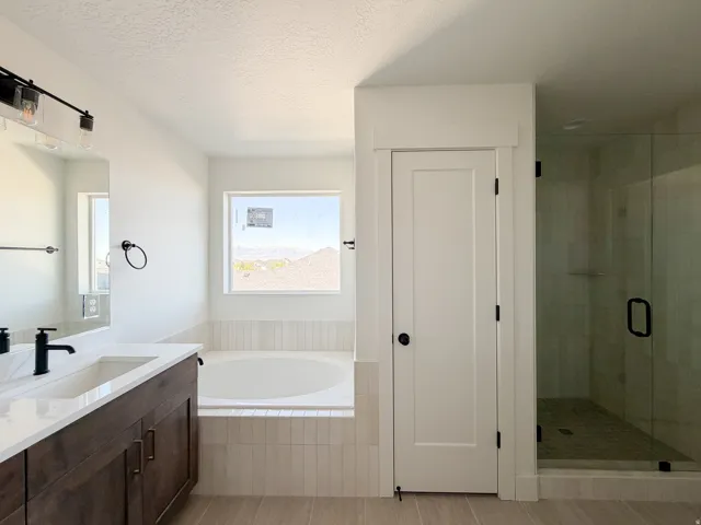 Well-appointed bathroom featuring a built-in soaking tub with vertical tile surround, a spacious glass-enclosed shower, a dual-sink vanity with dark wood-finish cabinetry, and a large window