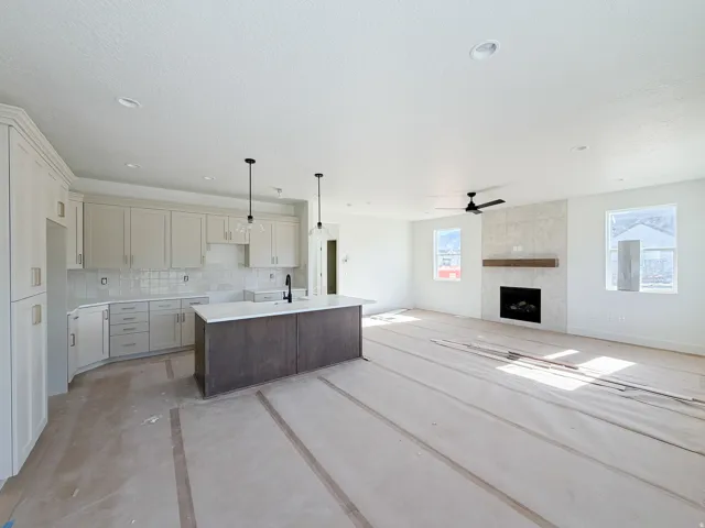 Open-concept kitchen and living area featuring a central island with a solid surface countertop, light-toned cabinetry, and a white subway tile backsplash