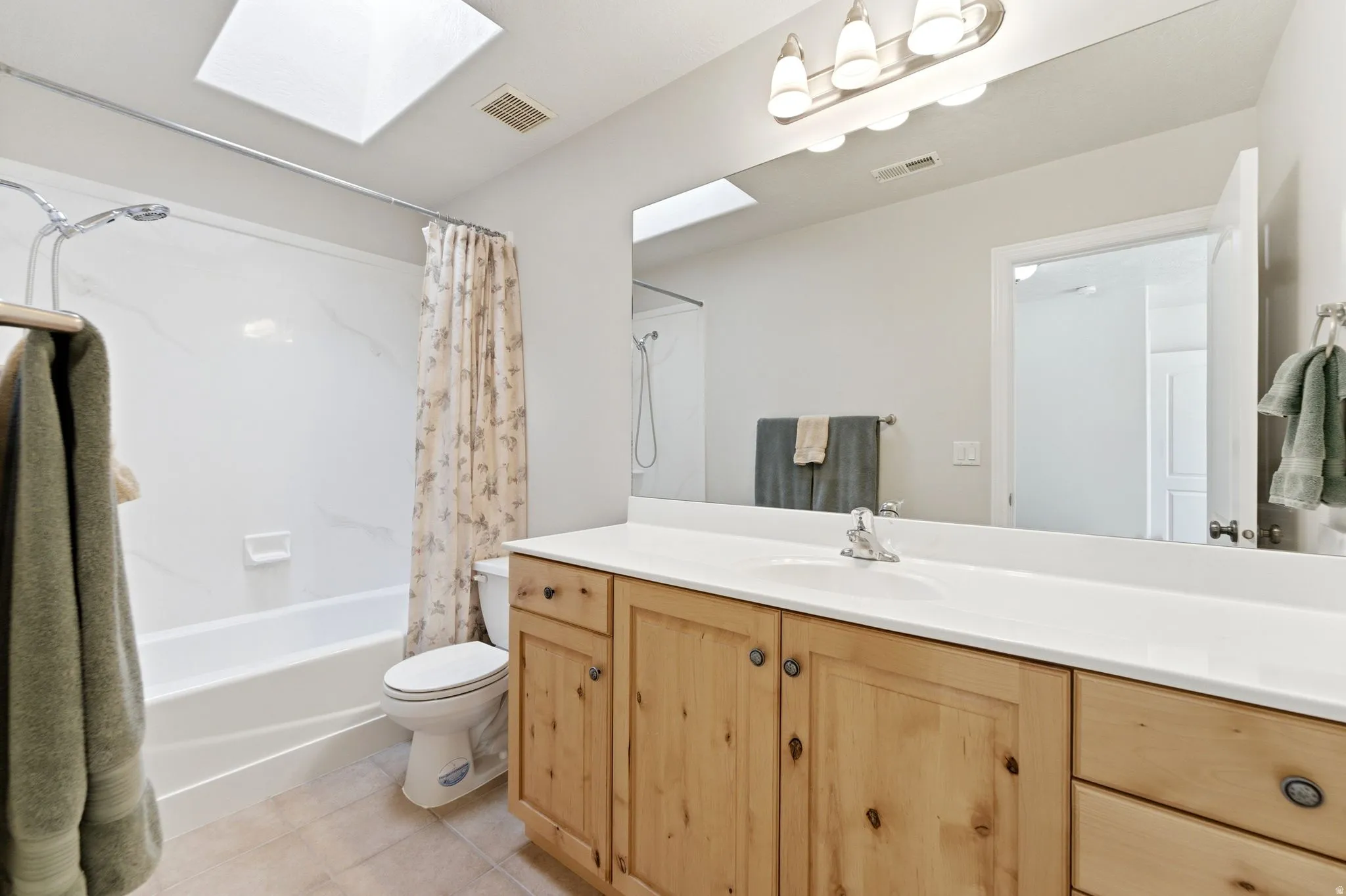 Full bathroom with vanity, shower / tub combo with curtain, light tile patterned floors, and a skylight