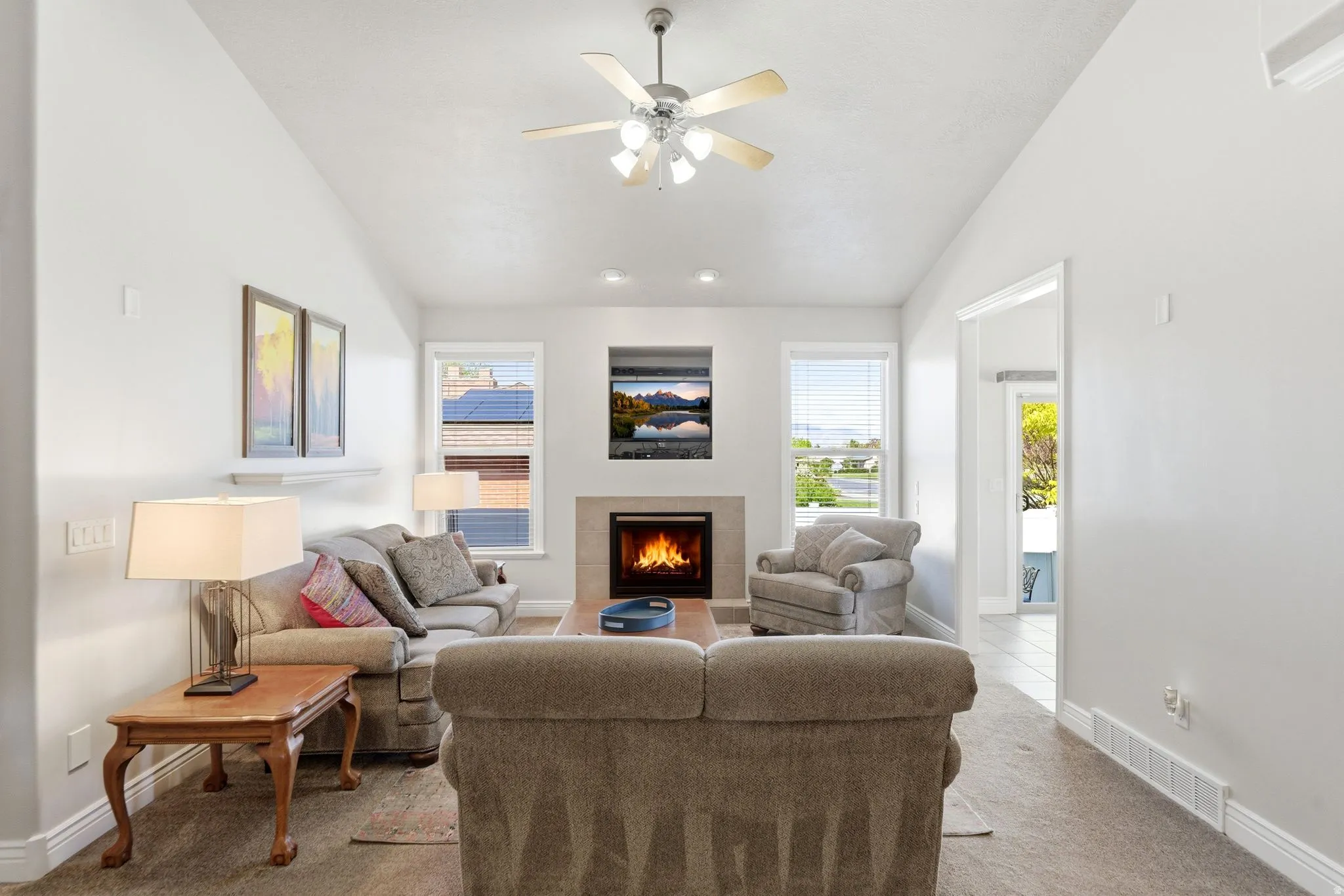Carpeted living area featuring vaulted ceiling, a tile fireplace, and ceiling fan