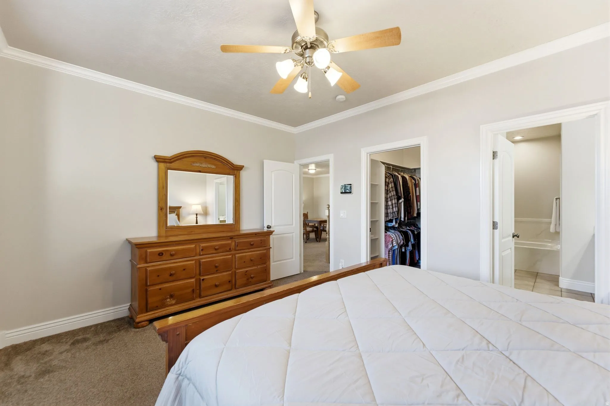Bedroom with carpet floors, crown molding, a ceiling fan, a walk in closet, and ensuite bath