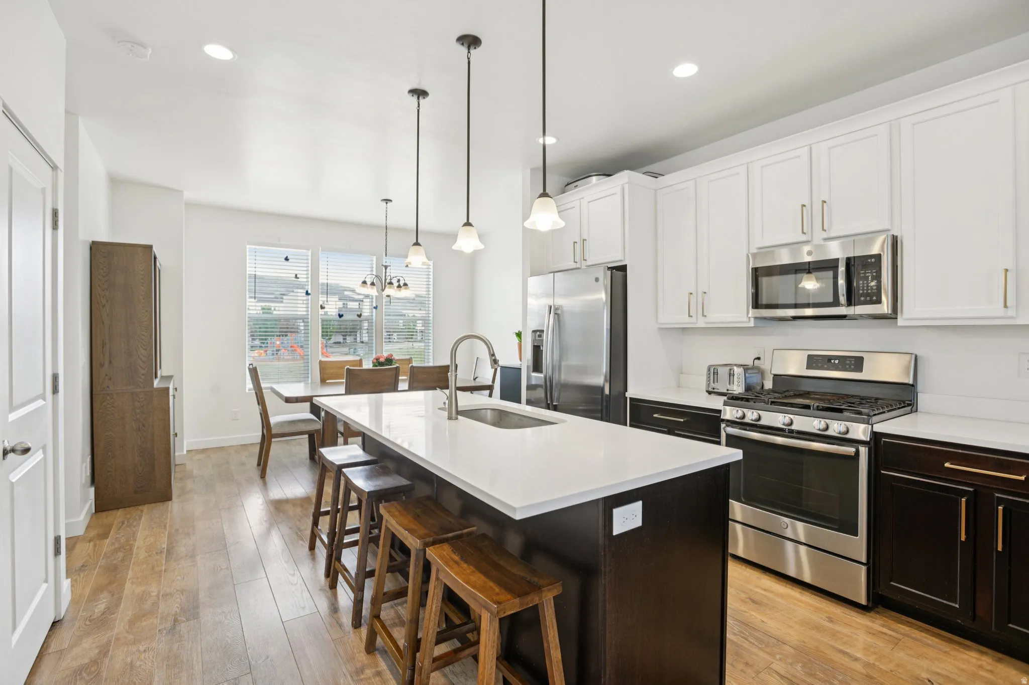 Dual tone kitchen featuring stainless steel appliances, a kitchen breakfast bar, dual tone cabinetry, a kitchen island with sink, and light wood-type flooring