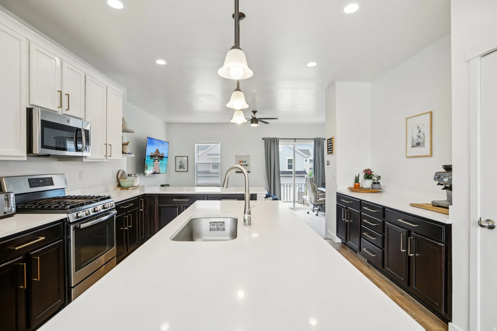 Kitchen with stainless steel appliances, hanging light fixtures, ceiling fan, two tone color scheme, and light wood finished floors