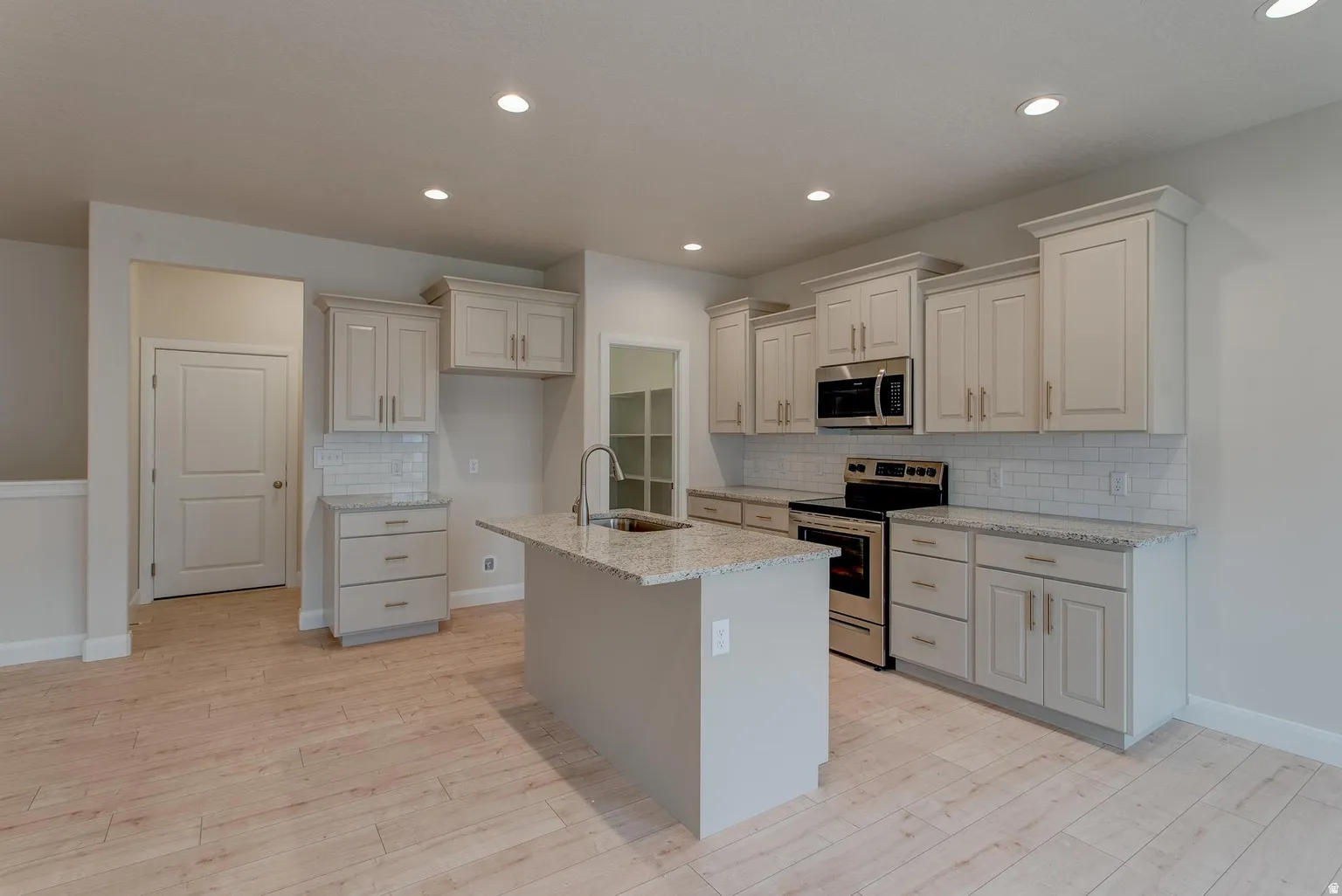 Kitchen featuring stainless steel appliances, light stone counters, tasteful backsplash, light wood-style floors, and a center island with sink