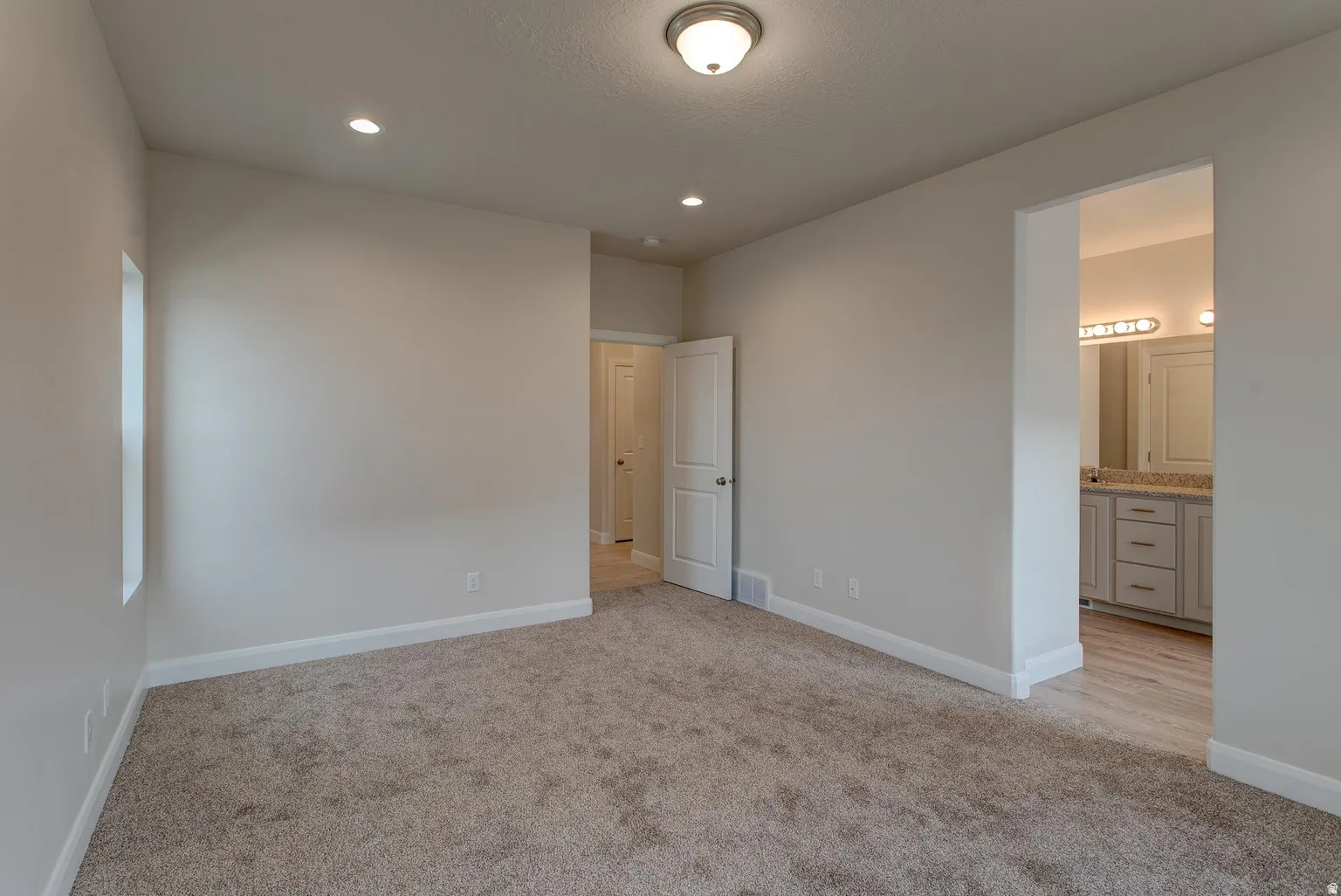 Unfurnished bedroom with light colored carpet, recessed lighting, and ensuite bathroom