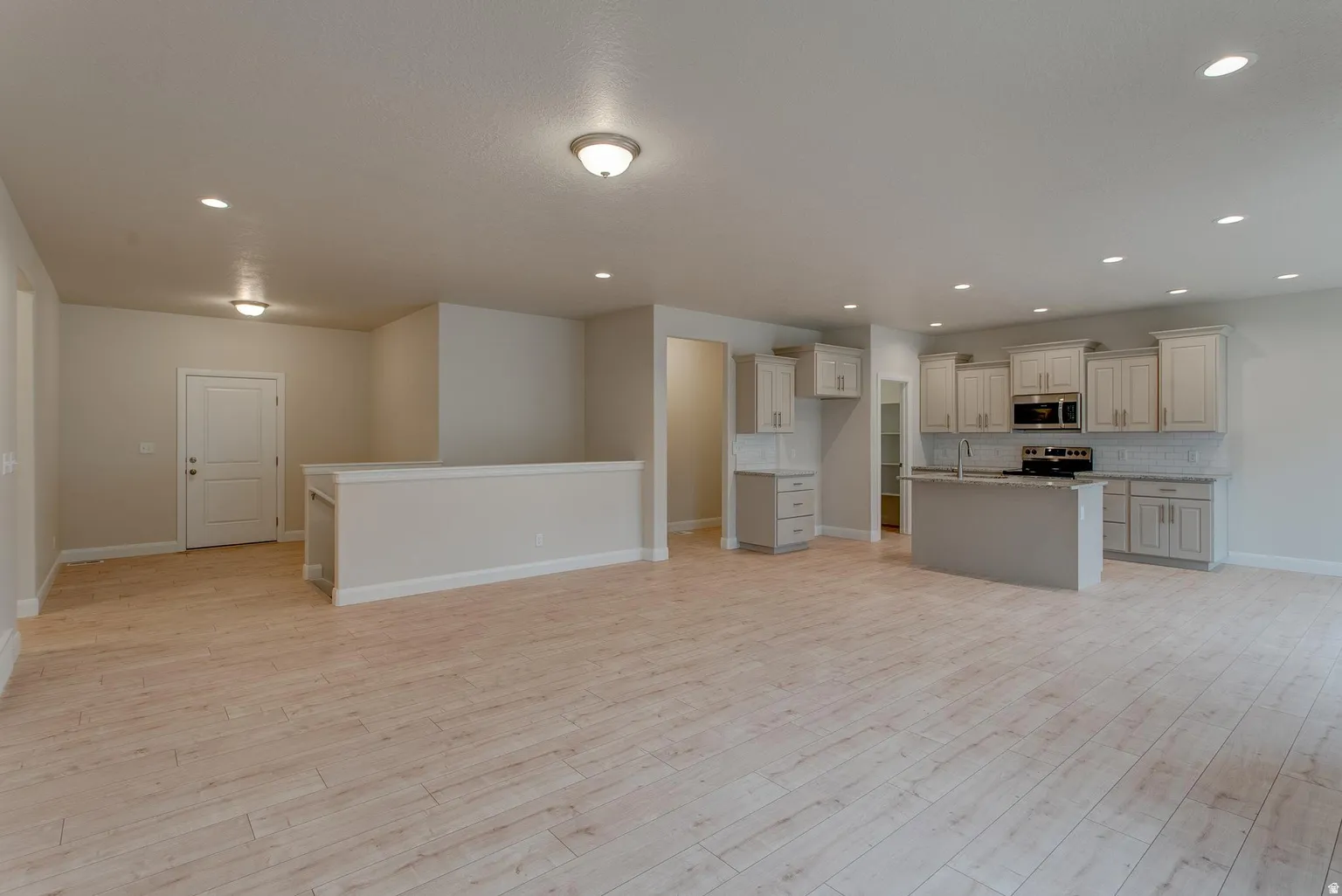 Kitchen featuring open floor plan, an island with sink, light wood finished floors, backsplash, and stainless steel appliances