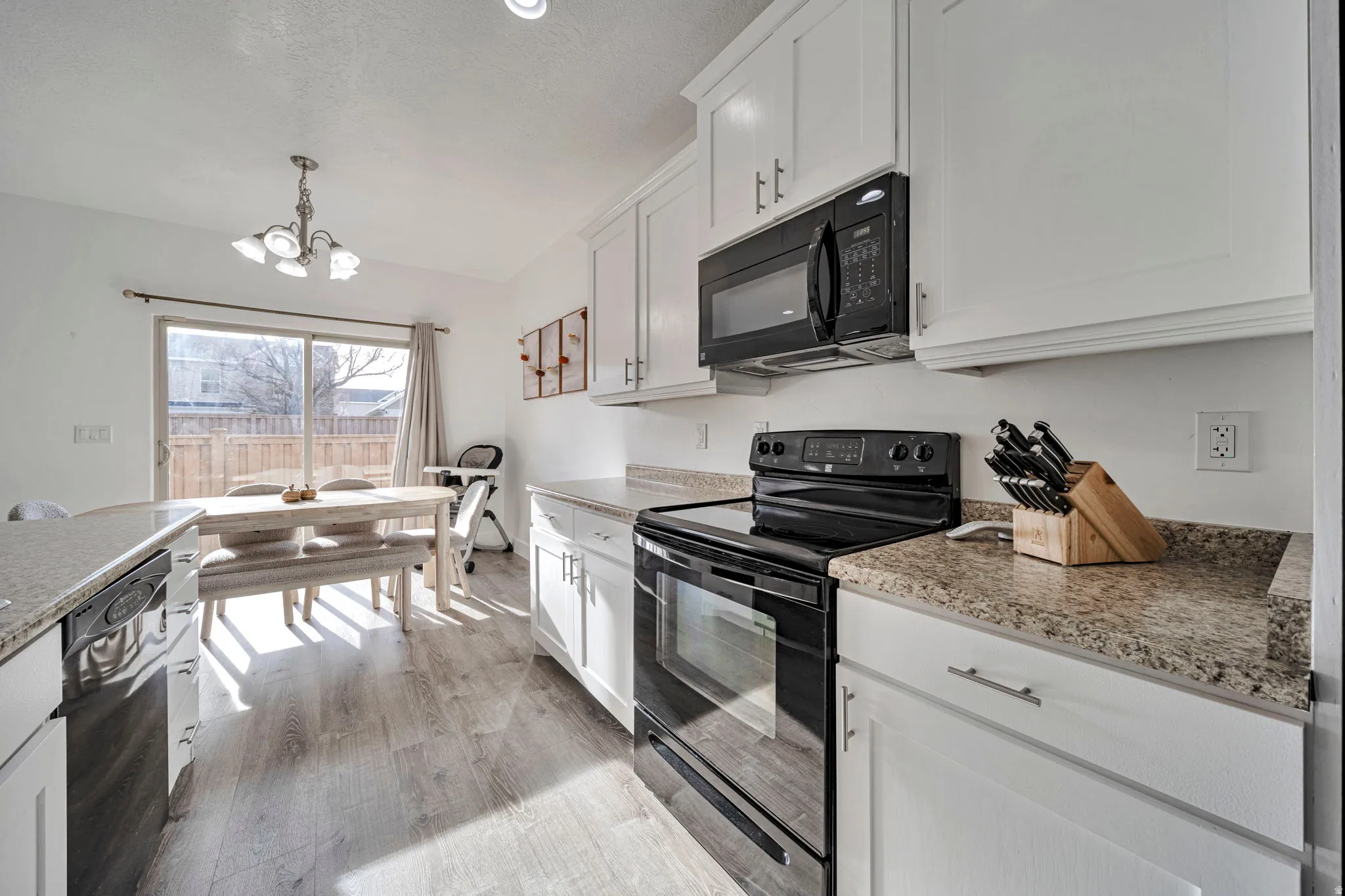 Kitchen with black appliances, white cabinetry, suspended lighting, and light wood-style floors