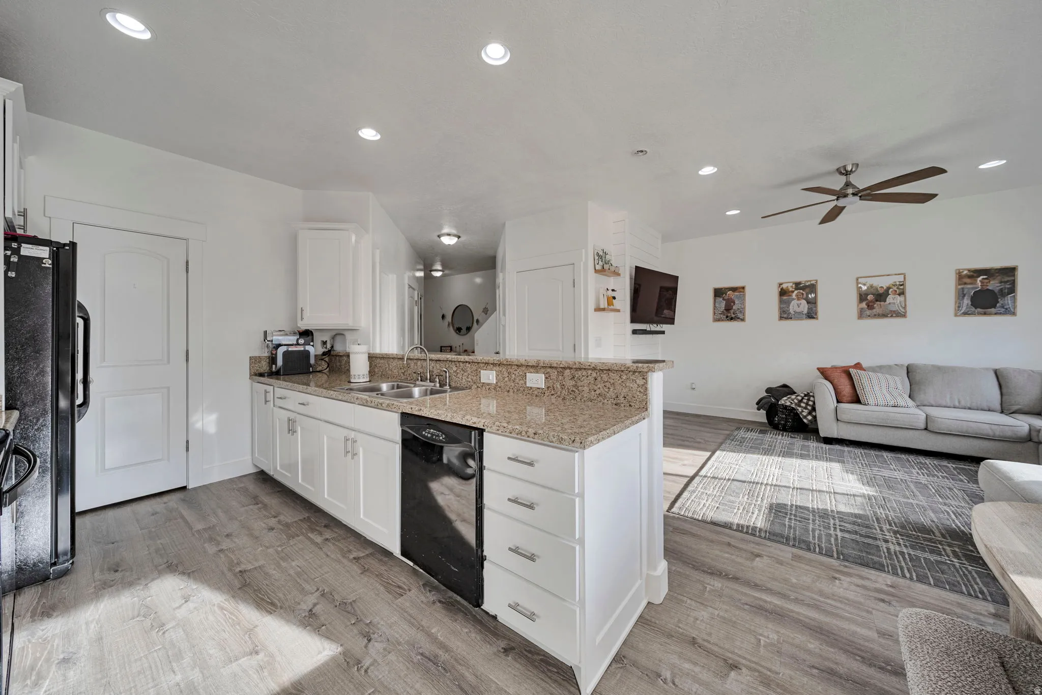 Kitchen featuring a peninsula, white cabinetry, open floor plan, light stone countertops, and light wood-style flooring