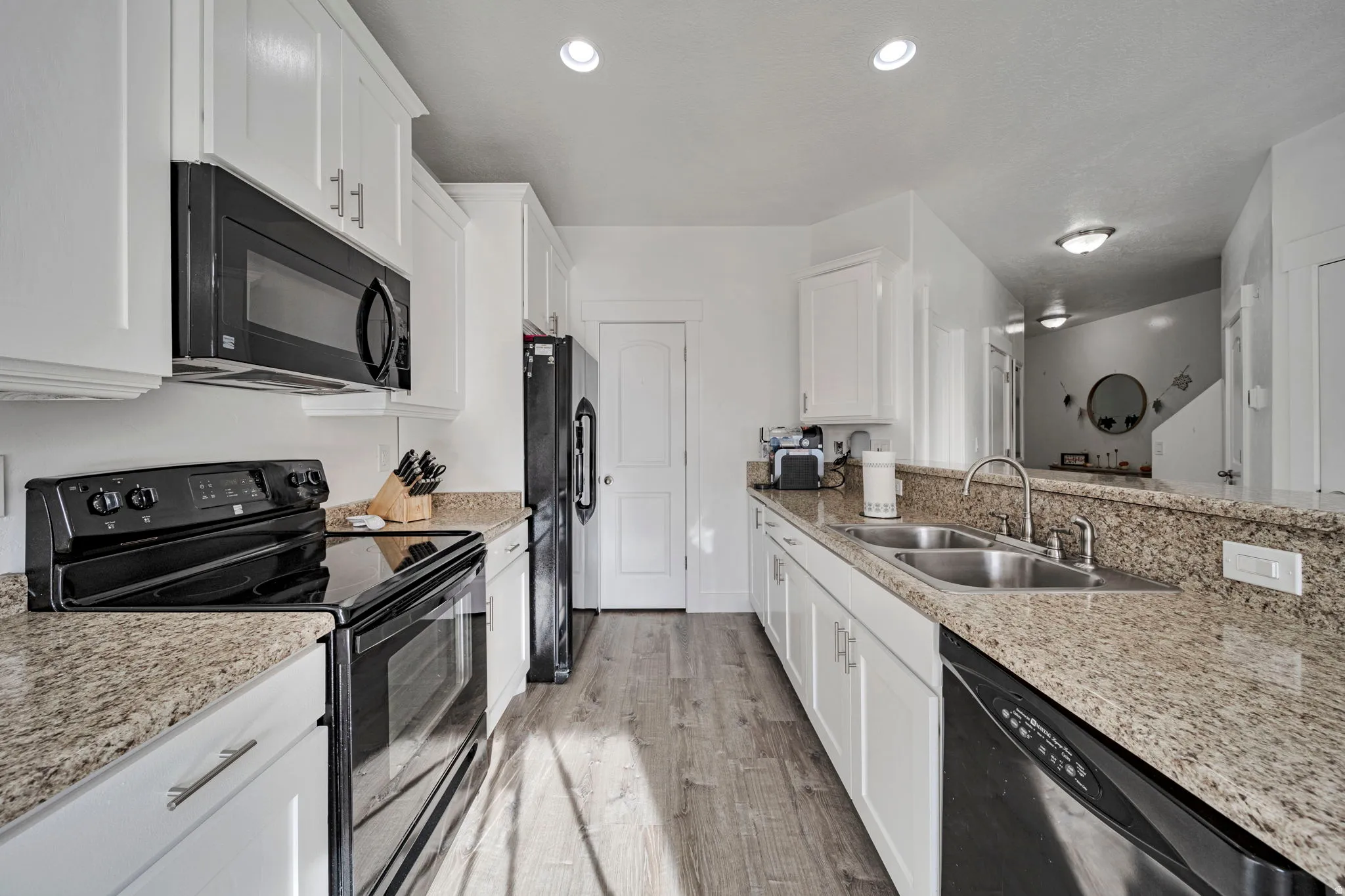 Kitchen featuring black appliances, white cabinetry, and light stone countertops