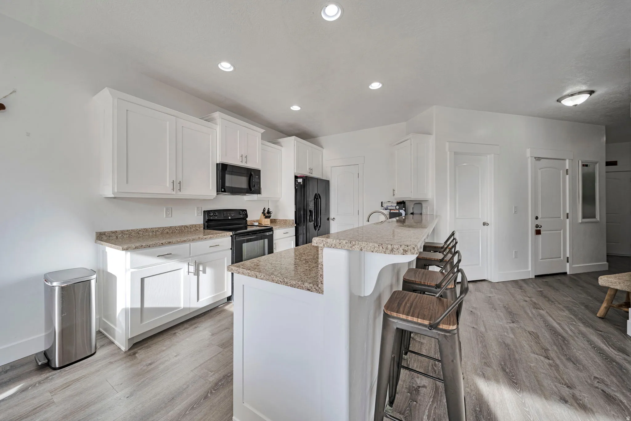 Kitchen with white cabinetry, a breakfast bar, black appliances, light wood-style flooring, and a peninsula