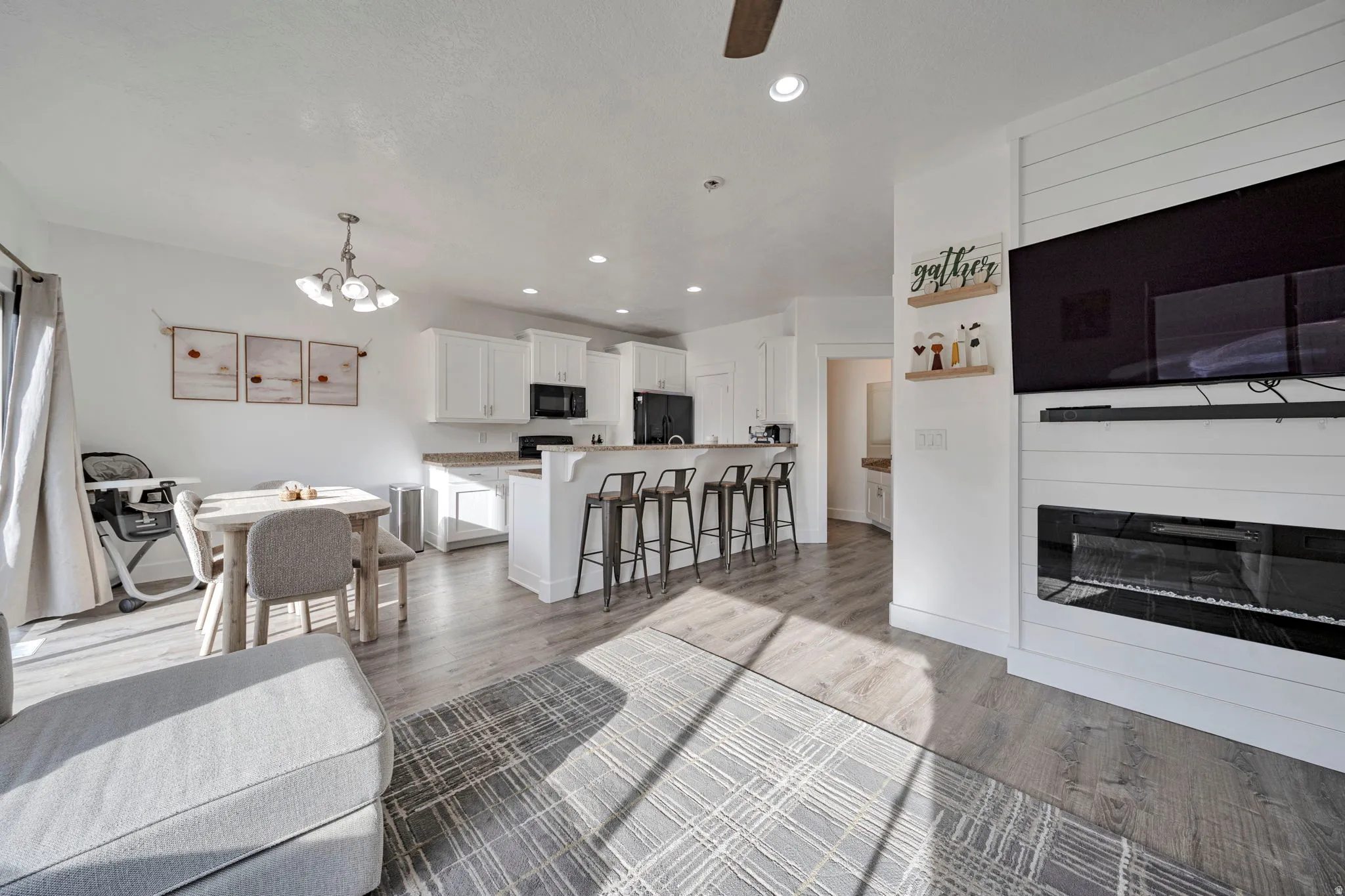 Living room featuring light wood-style floors, a chandelier, ceiling fan, and a glass covered fireplace