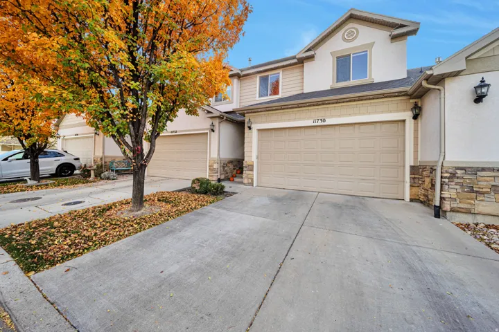 View of front of home with stone siding, driveway, an attached garage, and stucco siding