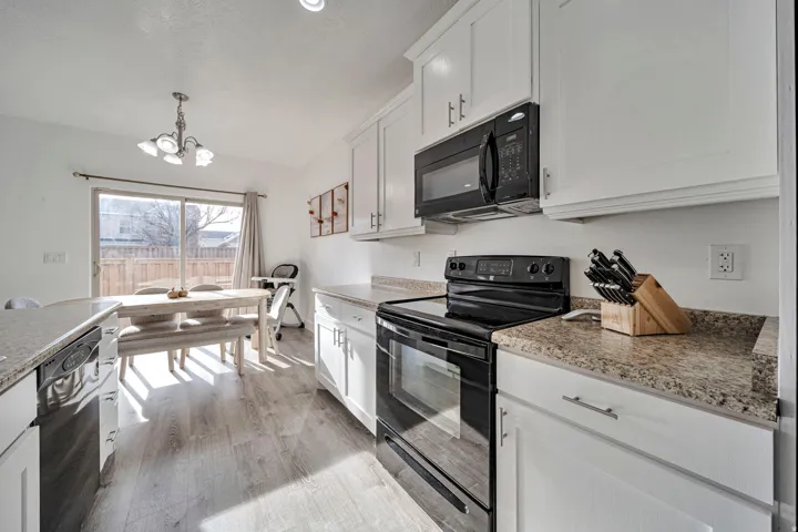 Kitchen with black appliances, white cabinetry, suspended lighting, and light wood-style floors