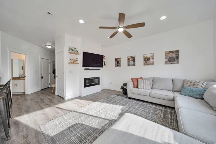 Living area featuring light wood-type flooring, a fireplace, ceiling fan, and recessed lighting