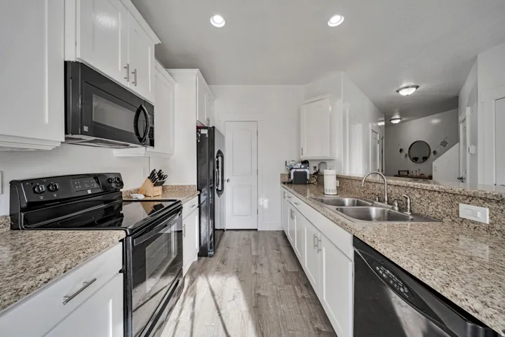 Kitchen featuring black appliances, white cabinetry, and light stone countertops