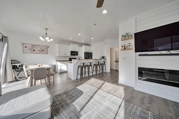 Living room featuring light wood-style floors, a chandelier, ceiling fan, and a glass covered fireplace
