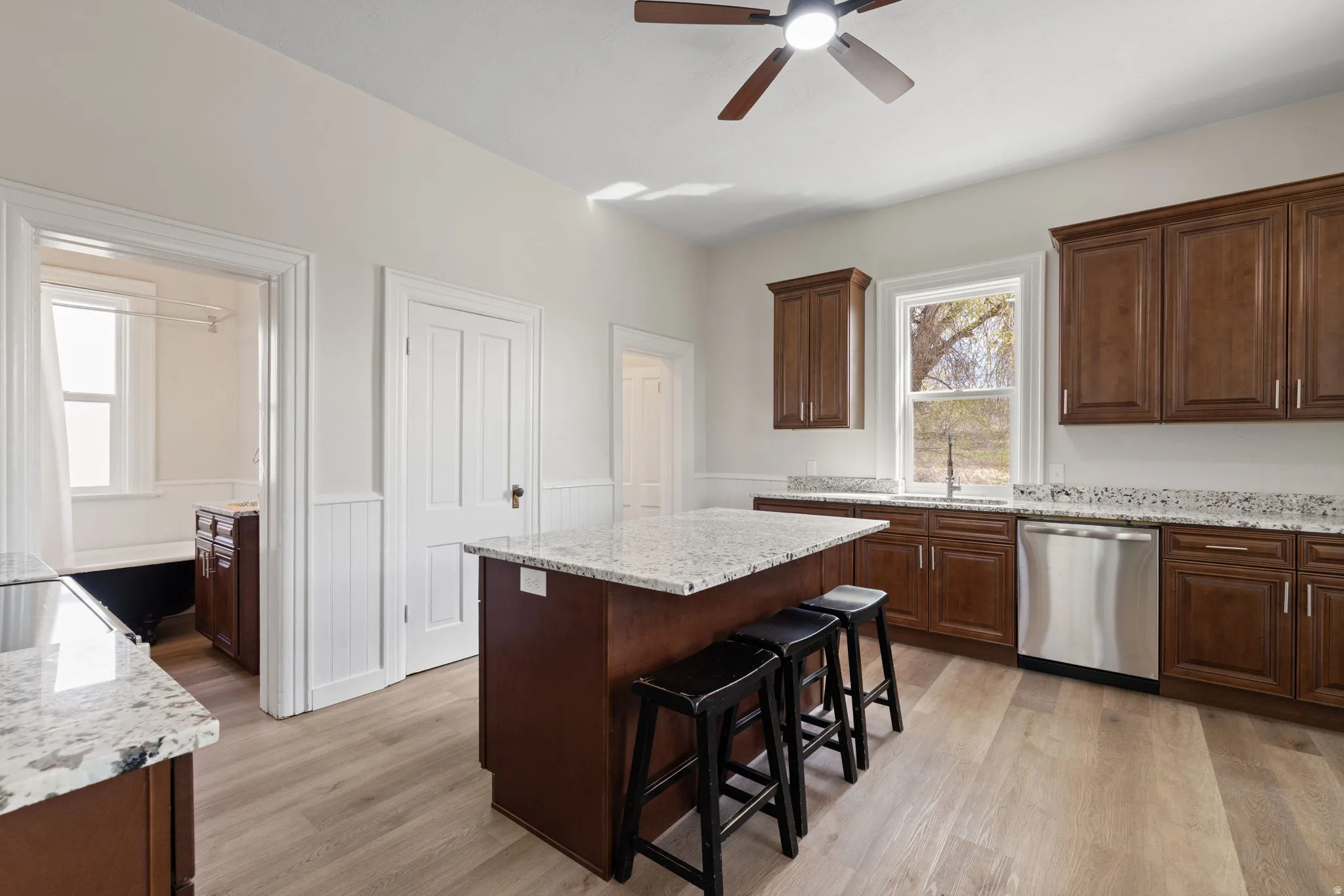 Kitchen with light stone countertops, wainscoting, ceiling fan, dishwasher, and light wood-type flooring