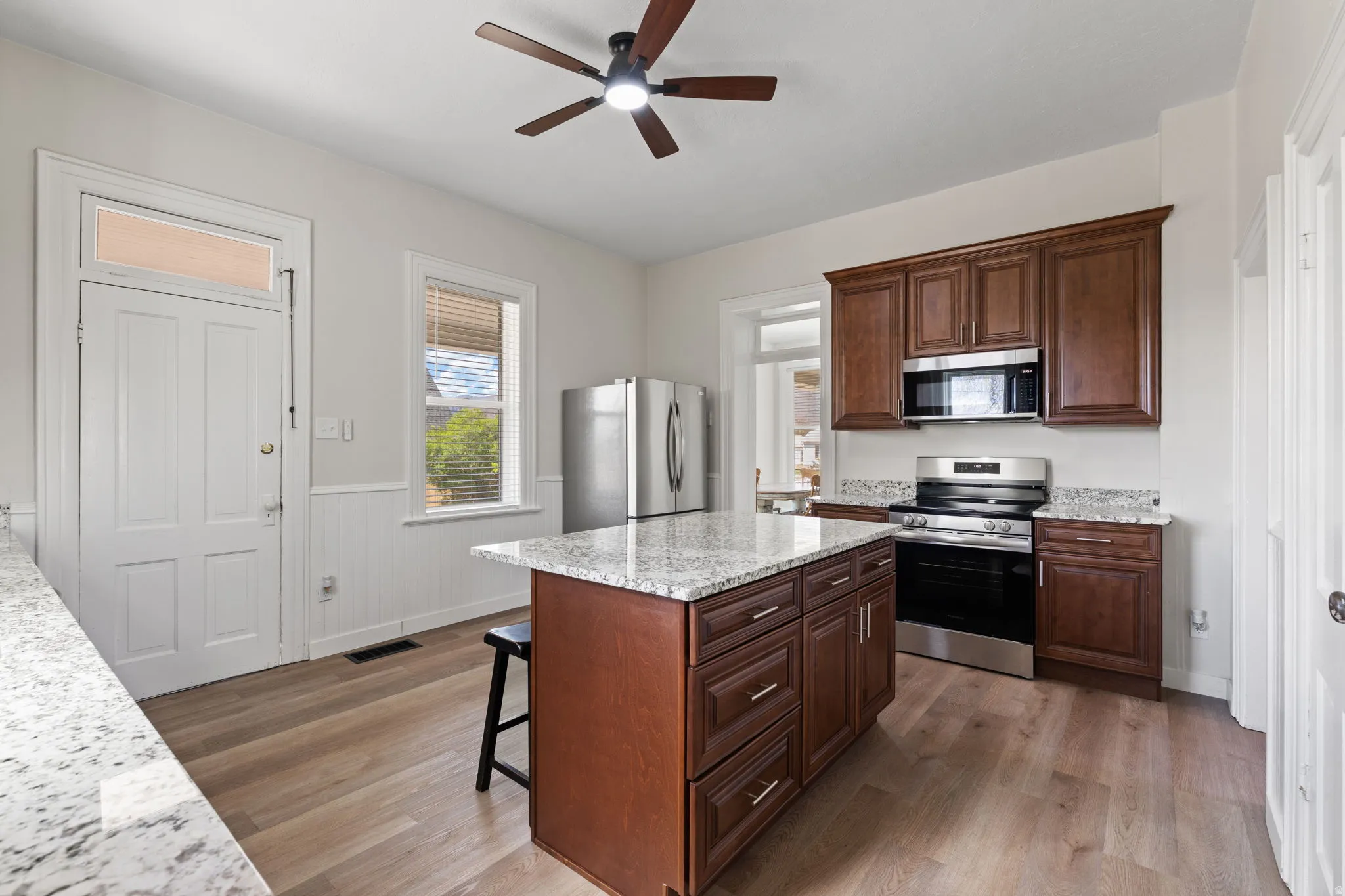 Kitchen with stainless steel appliances, a breakfast bar area, light wood-style flooring, a ceiling fan, and wainscoting