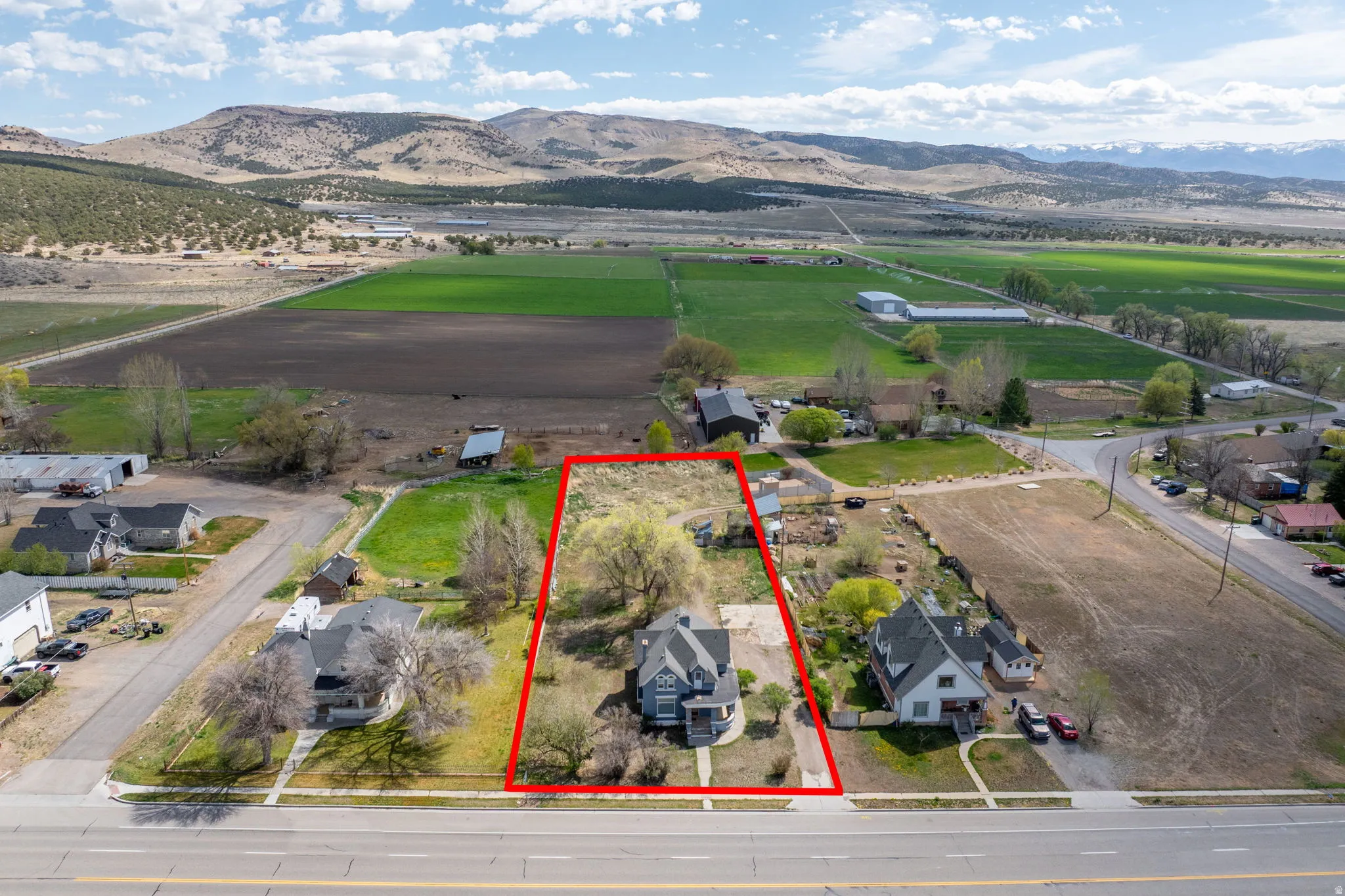Aerial view of sparsely populated area with a mountainous background, property parcel outlined, and nearby suburban area