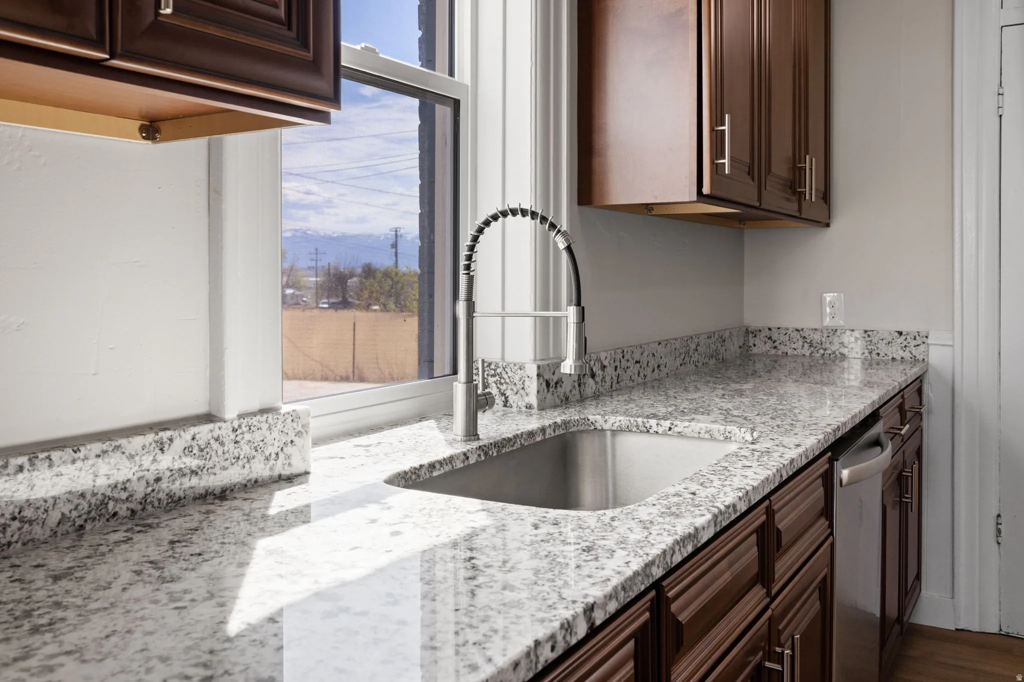 Kitchen with light stone countertops, dark wood finish cabinets, and stainless steel dishwasher
