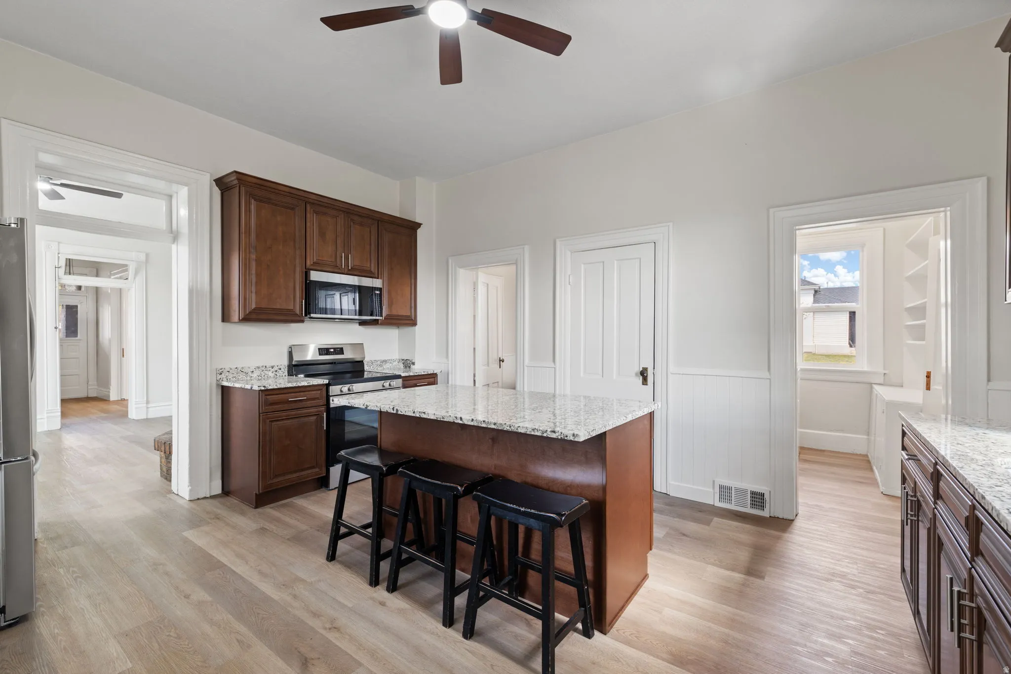 Kitchen with ceiling fan, stainless steel appliances, light stone countertops, a kitchen breakfast bar, and a center island
