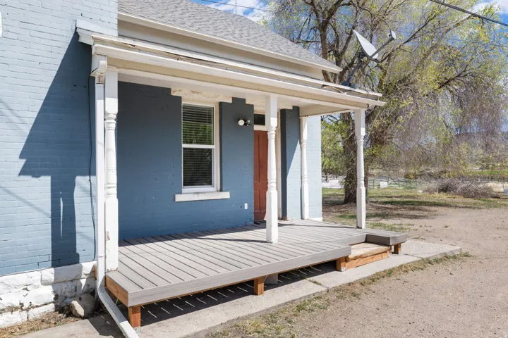 View of exterior entry with a porch, roof with shingles, and brick siding