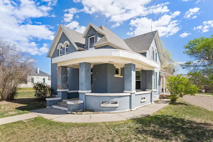 Victorian house featuring brick siding, roof with shingles, a large porch, and a front lawn