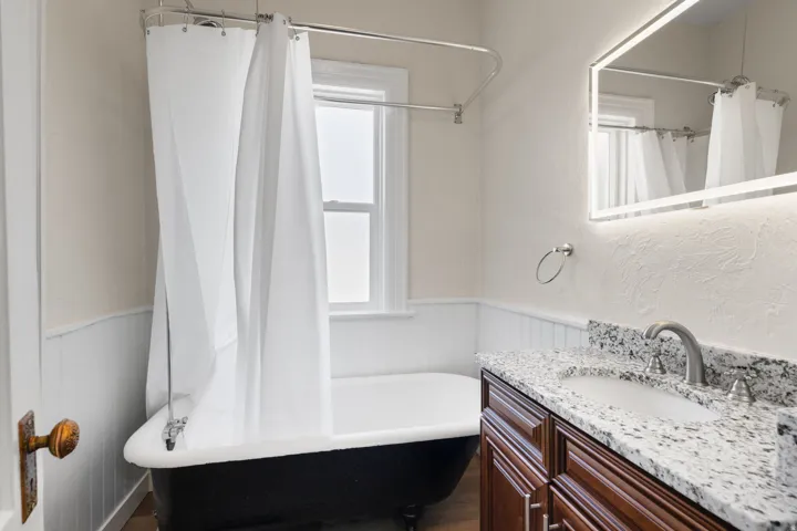Bathroom featuring vanity, a wainscoted wall, and a combined bath / shower with freestanding tub