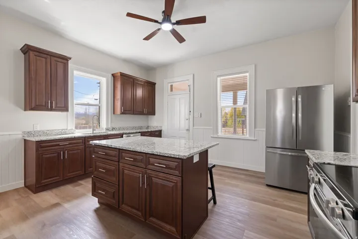 Kitchen featuring a wainscoted wall, freestanding refrigerator, light stone counters, a center island, and a breakfast bar area
