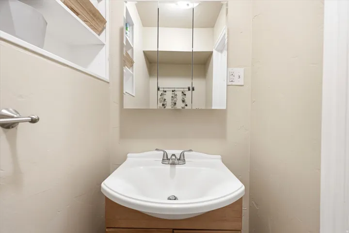 Pedestal sink with chrome faucet, complemented by a medicine cabinet with mirrored doors