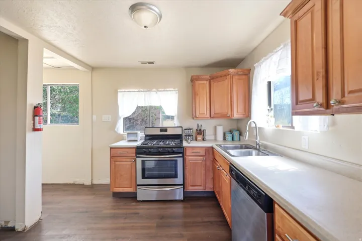 Kitchen featuring wood-finish flooring, light-toned cabinetry, a stainless steel gas range, a stainless steel dishwasher, and a double basin sink