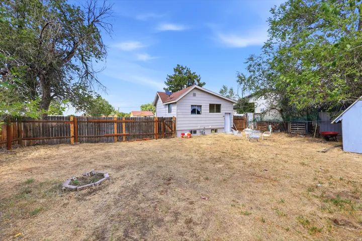 Spacious backyard featuring a wood privacy fence, mature trees, a small shed, and a built-in fire pit