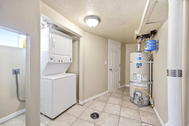 Dedicated utility area featuring a stacked washer and dryer, tiled flooring, and a water heater