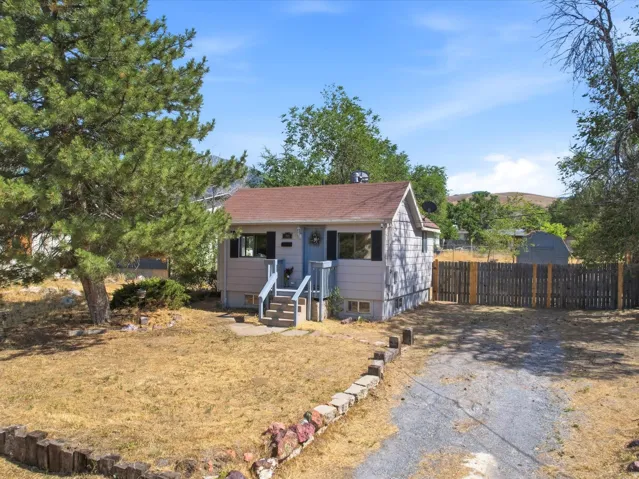 Single-story residence featuring a gravel driveway, mature trees, and a fenced backyard