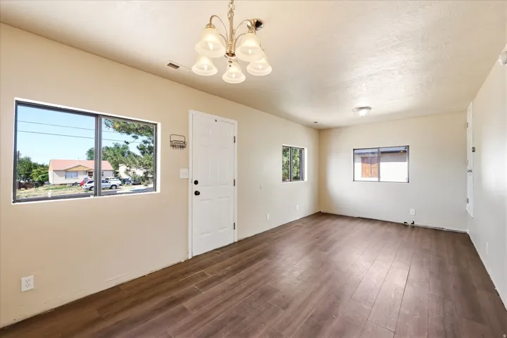 Open living area featuring wood-finish flooring, light-toned walls, multiple windows, and a multi-light chandelier