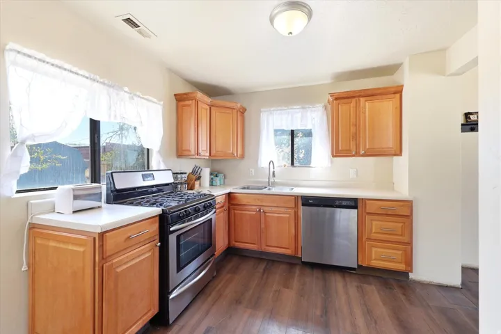 Kitchen featuring wood-finish flooring, light wood cabinetry, light-toned countertops, and stainless steel appliances including a gas range and dishwasher