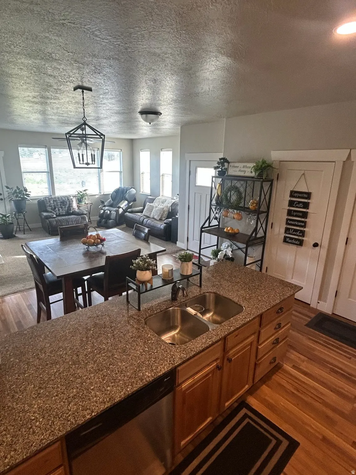 Kitchen with open floor plan, dark wood-style flooring, stainless steel dishwasher, wood finish cabinets, and a textured ceiling