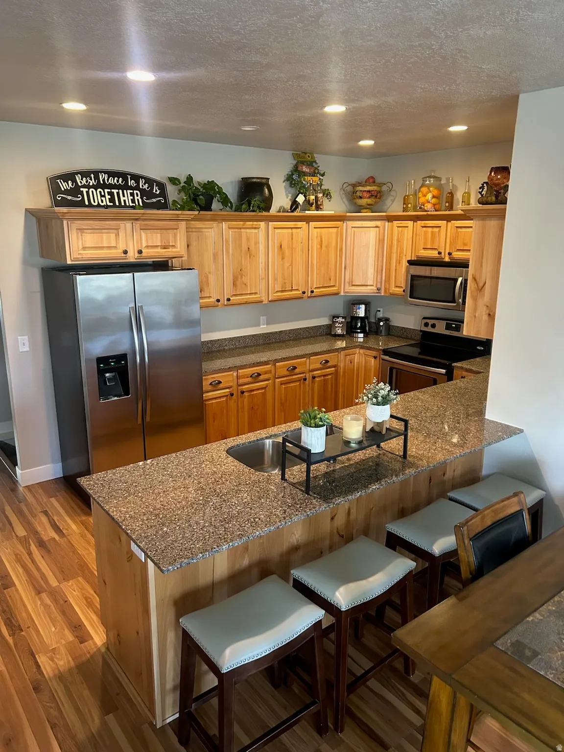 Kitchen featuring a kitchen breakfast bar, dark stone counters, a textured ceiling, stainless steel appliances, and recessed lighting