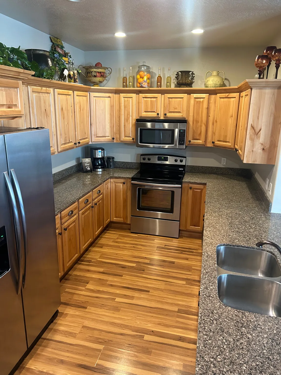Kitchen with stainless steel appliances, dark stone countertops, light wood finished floors, a textured ceiling, and wood finish cabinets