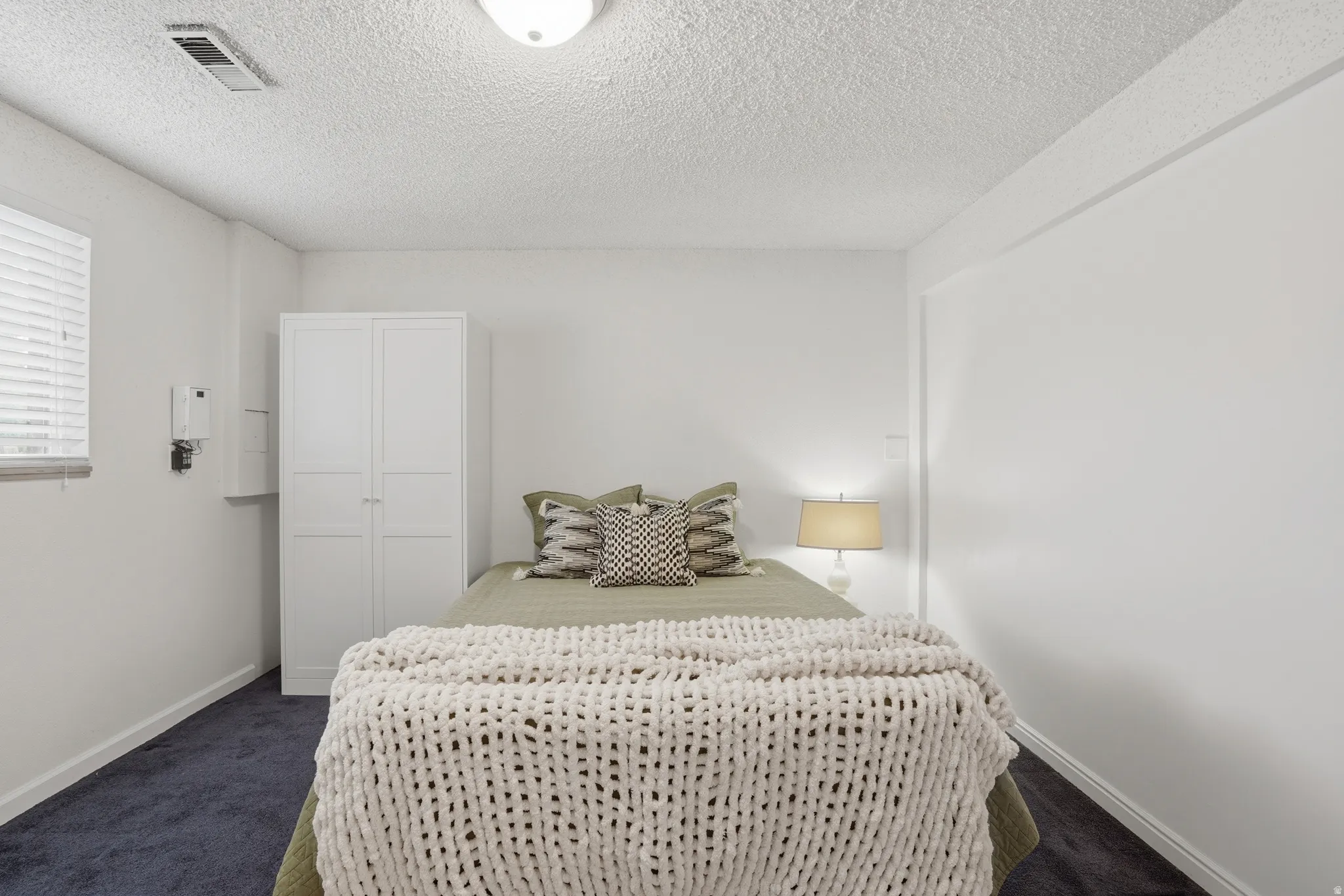 Bedroom with dark colored carpet and a textured ceiling