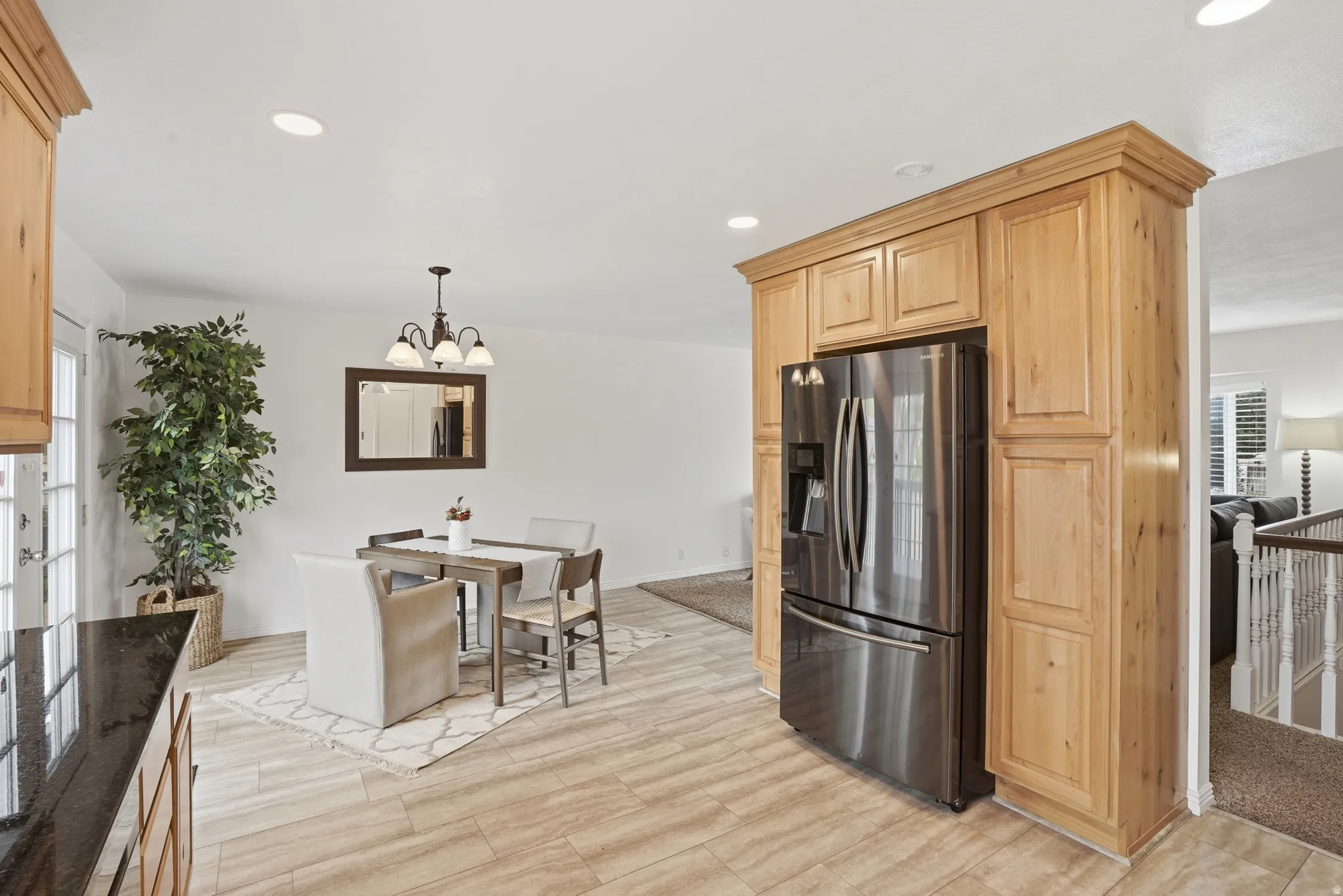 Kitchen featuring stainless steel fridge with ice dispenser, light wood finish cabinets, light wood finished floors, and a chandelier
