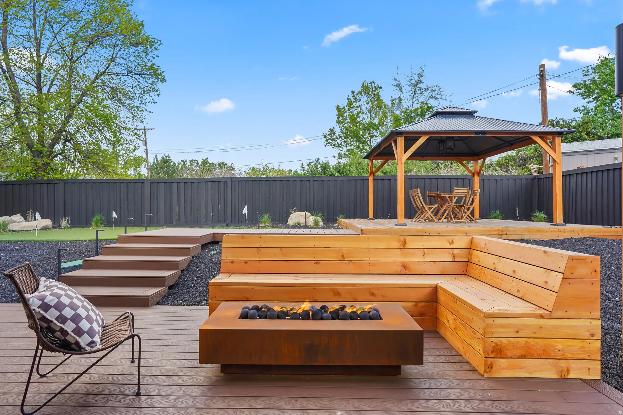 Wooden deck with a fenced backyard, a gazebo, an area to practice putting, and a fire pit