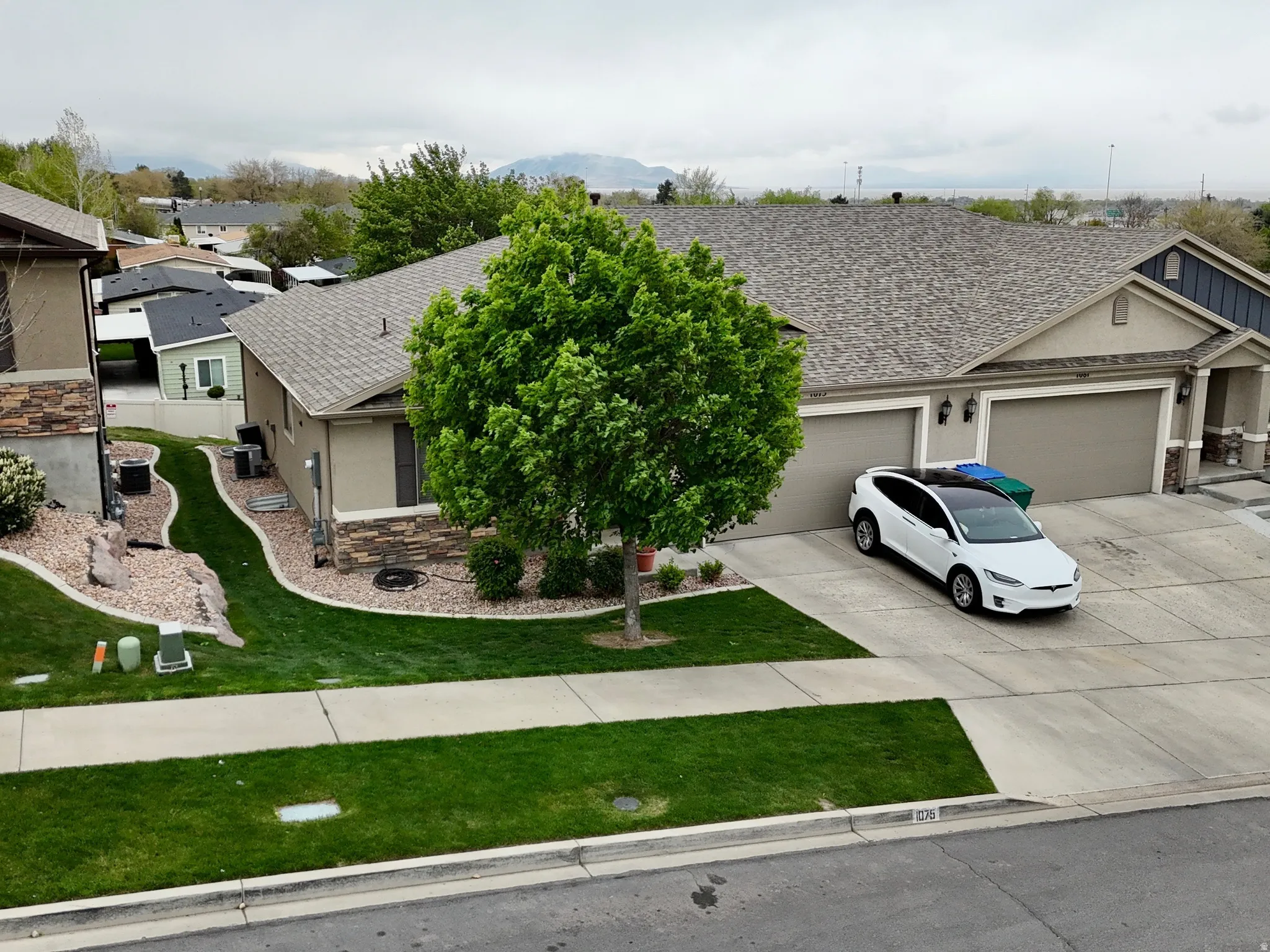 View of front of property with stone siding, an attached garage, driveway, stucco siding, and a front yard
