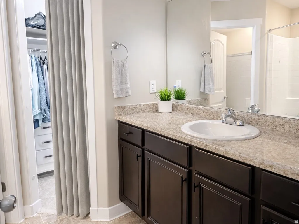 Bathroom featuring a spacious closet, vanity, light tile patterned floors, and a shower