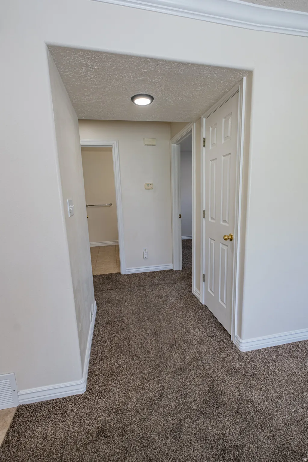 Corridor featuring a textured ceiling and dark carpet