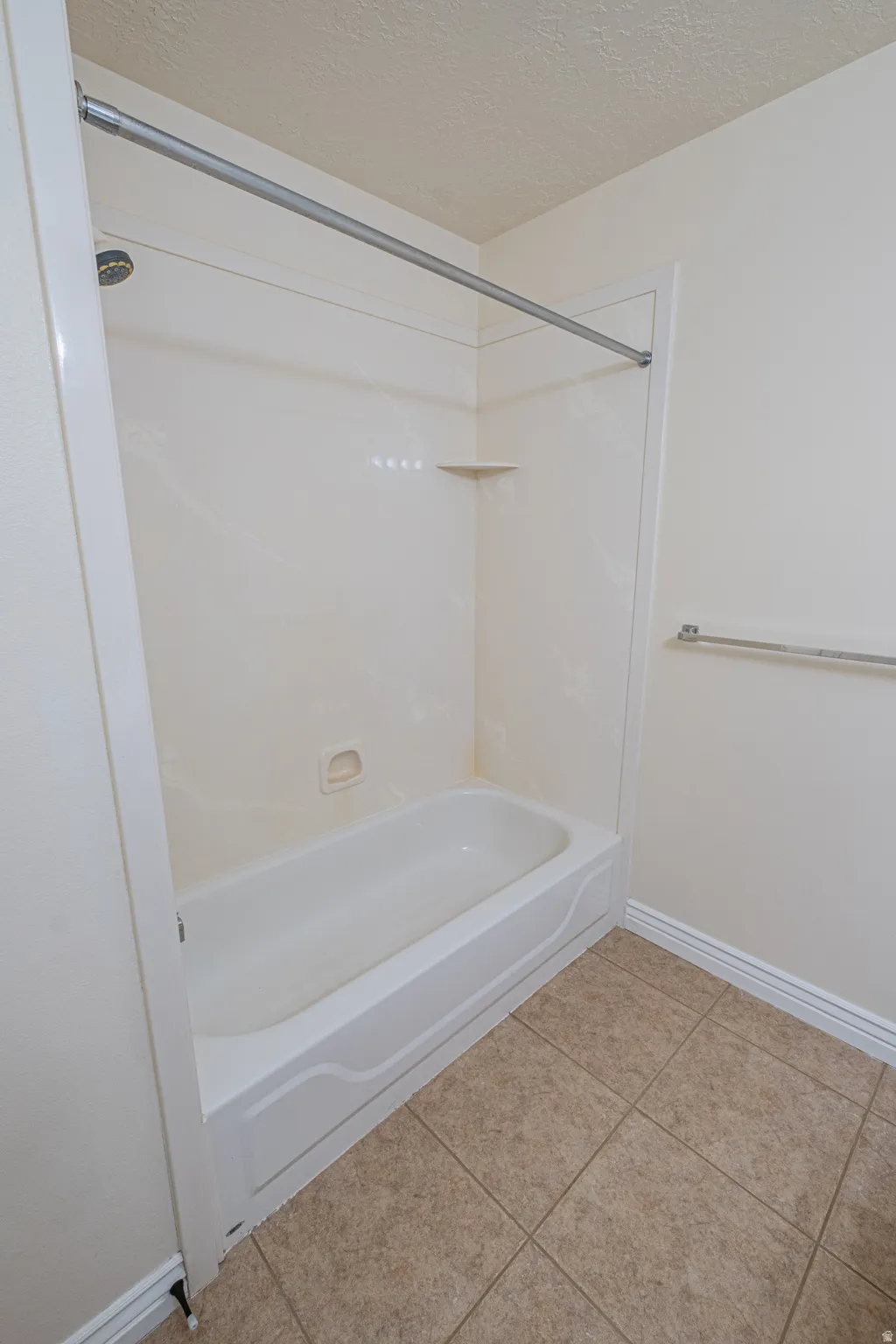 Full bath with a textured ceiling, light tile patterned flooring, and shower / bath combination